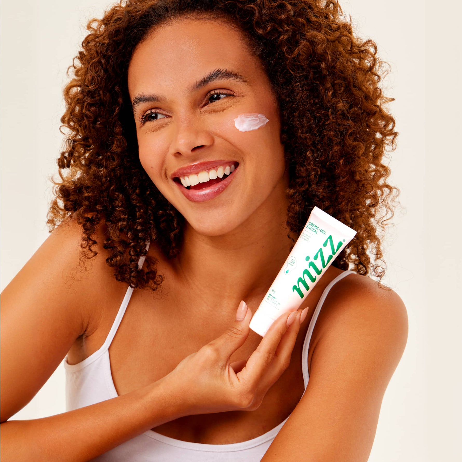 Mulher cacheada sorridente aplica Creme-gel Facial Hidratante 72h Mizz no rosto