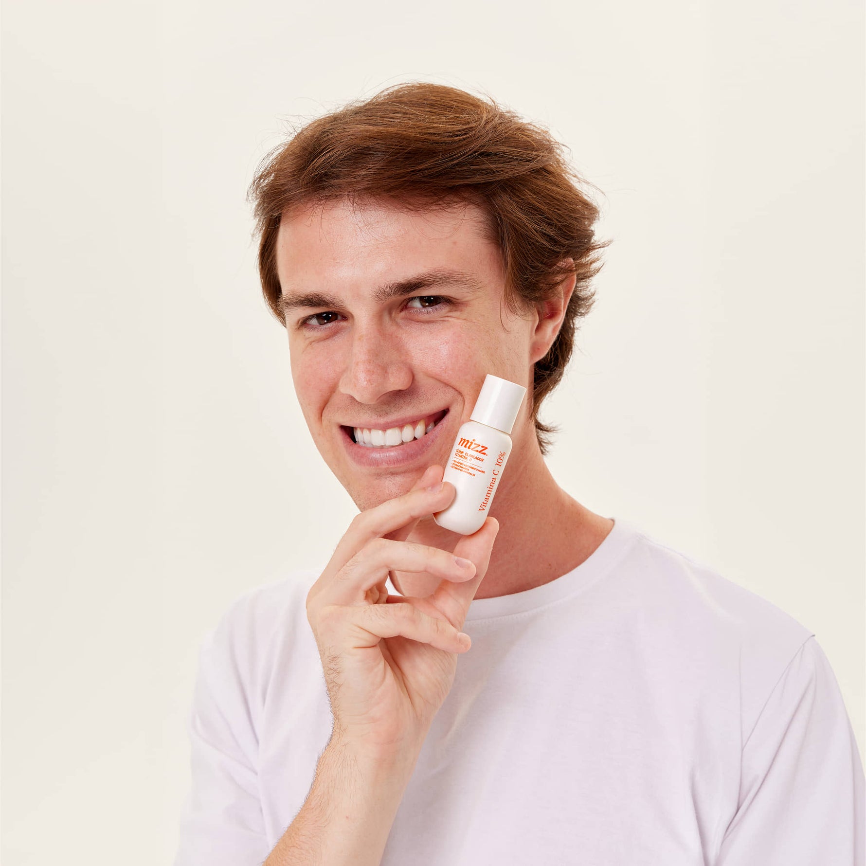 Jovem sorrindo de camiseta branca segurando Sérum Vitamina C 10% Mizz com detalhes laranja