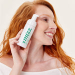 Mulher ruiva sorridente segurando frasco de espuma de limpeza facial Mizz com bomba